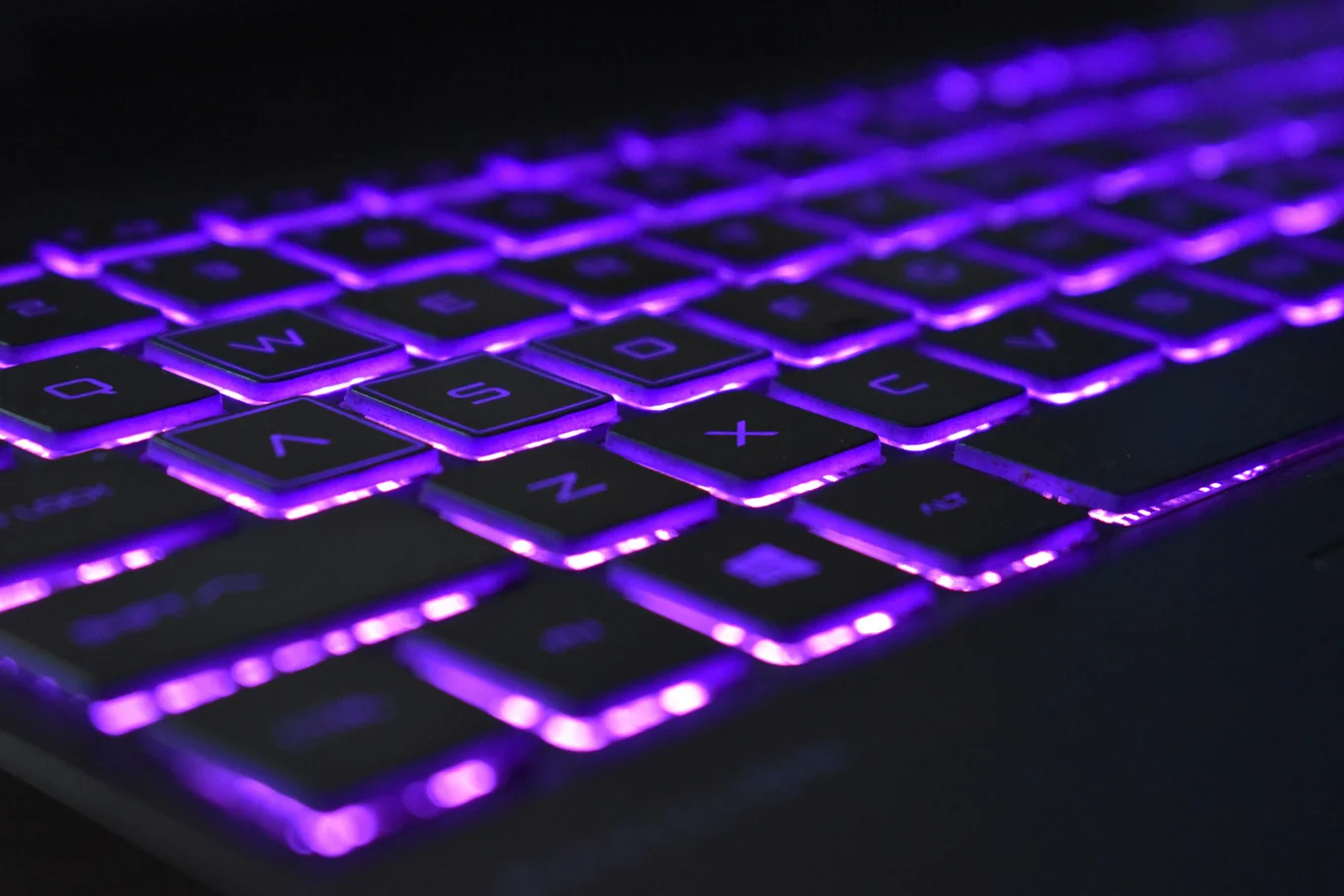 Purple backlit computer keyboard, angled view.