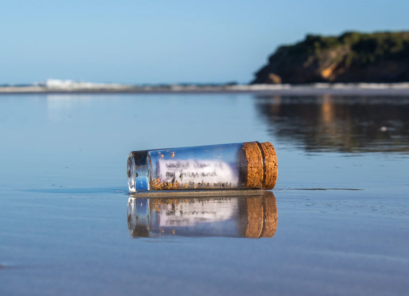 Bottle with cork on wet sand, text inside, ocean.