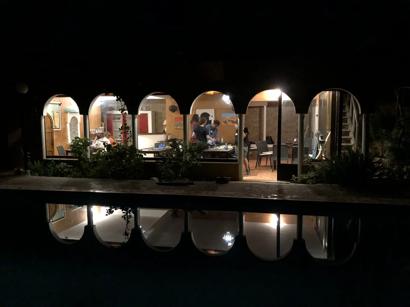 Room with arched windows, people inside, plants outside.