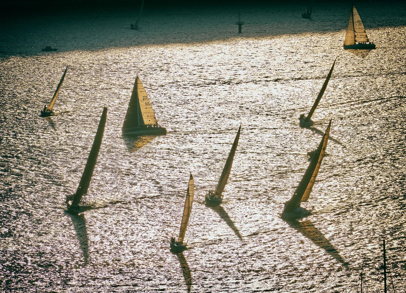 Sailboats on shimmering water, casting long shadows.