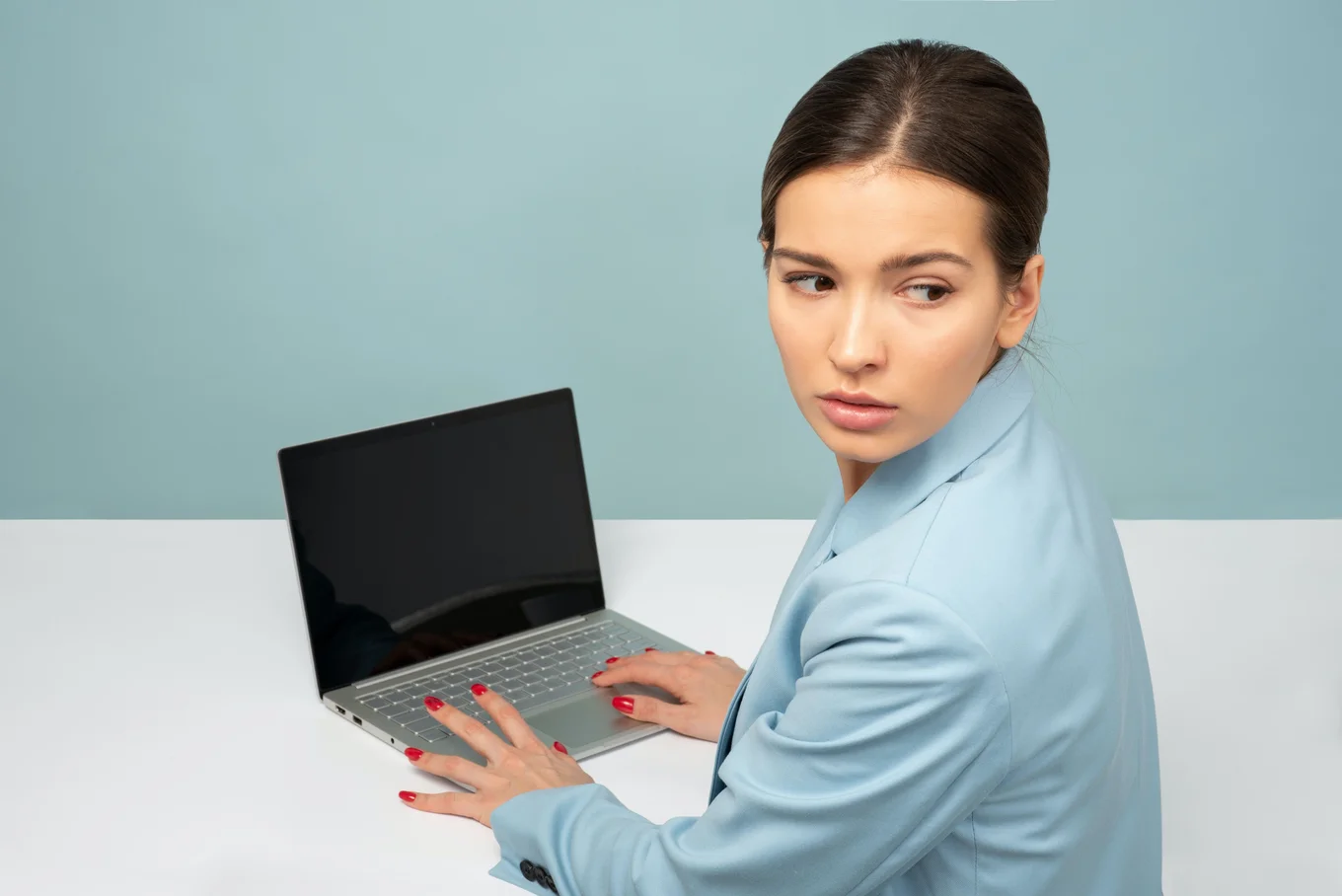 Person in blue suit using a laptop, blue background.